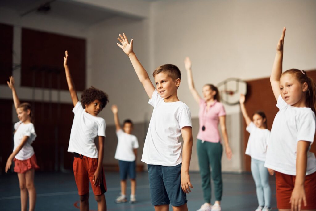 Group,Of,Elementary,Students,With,Raised,Arms,Exercising,On,Pe